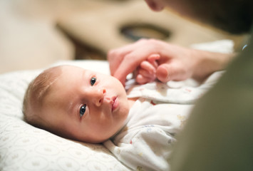 Newborn baby lying on bed, unrecognizable father stroking her head.