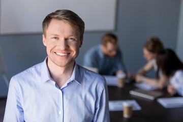 Portrait of smiling middle-aged male employee posing during company team meeting in boardroom,...
