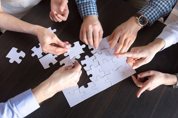 Top close up view of diverse employees assembling jigsaw puzzle trying to find best business solution, workers engaged in teambuilding practicing unity and support. Concept of successful cooperation