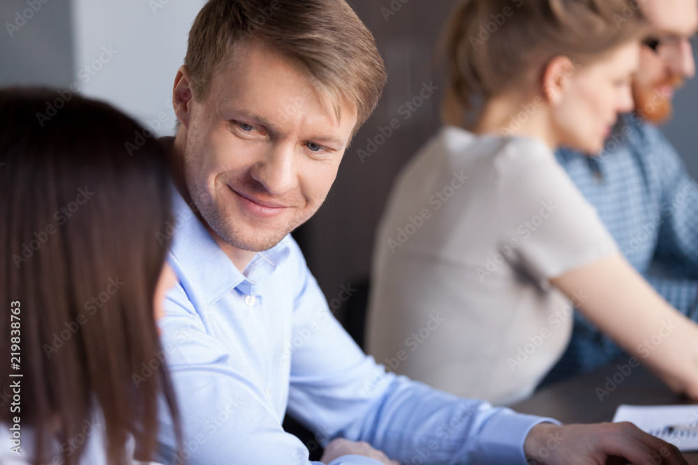 Wall mural Smiling millennial man look at female colleague while working together in office, interested male employee listen attentively to woman coworker, engaged in teambuilding activity. Cooperation concept