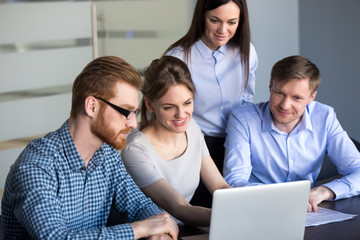 Smiling employees looking at laptop excited by company growing statistics and market success,...