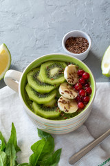 Breakfast spinach smoothie bowl with kiwi, banana, cranberries and flax seeds.