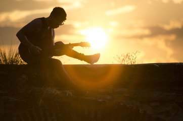 Man performs on electric guitar on old Roman aqueduct during sunset.