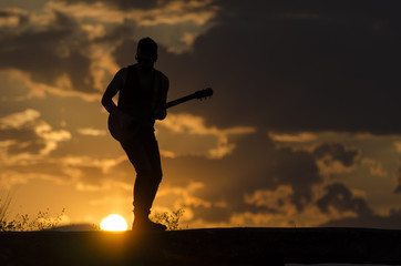 Man performs on electric guitar on old Roman aqueduct during sunset.