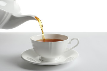 Pouring hot tea into porcelain cup on white background