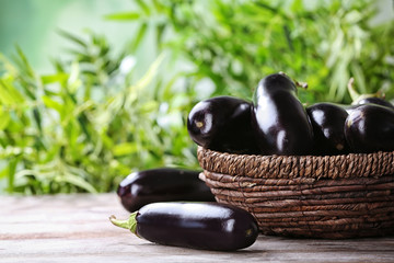 Bowl with ripe eggplants on table against blurred background