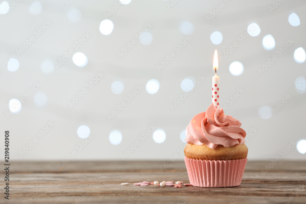 Wall mural delicious birthday cupcake with burning candle and space for text on blurred lights background