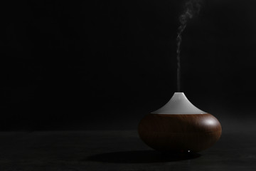 Aroma oil diffuser on table against dark background. Space for text