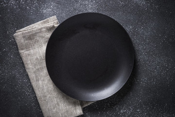 Black plate, cutlery and napkin on stone table top view.
