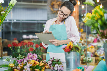 Portrait of young woman taking order by smartphone in flower shop