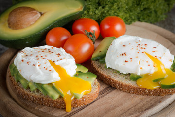 Avocado toast, cherry tomato and poached eggs on wooden background. Breakfast with vegetarian food, healthy diet concept.