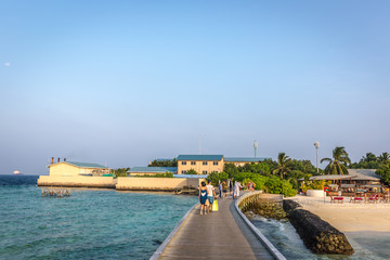Maldives, Feb 8th 2018 - Tourists enjoying the swimming pool area and the beach area of a resort in Maldives, afternoon lights, some trees and table.