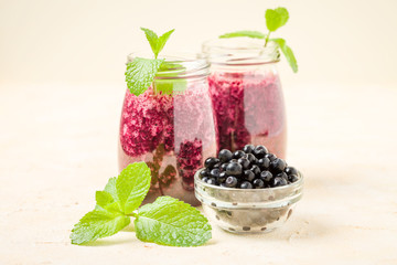 Blueberry smoothie decorated with fresh green mint leaves and raw ripe berries on yellow pastel background.