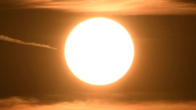 Extreme close up of the sun at sunset. Live action. Illuminated air dust spots accross the frame. Small heat air shimmering. HD, shot with long zoom lens.