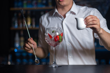 Wineglass filled with ice, strawberries and mint leafs on the bar counter with bartender on the background.