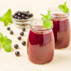 Currant smoothie decorated with fresh green mint leaves and raw ripe berries on yellow pastel background.