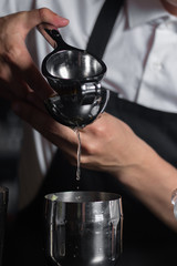 Barmens hands squeezes lemon juice into a chilled shaker on the bar counter.