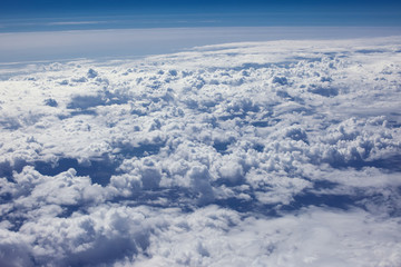 Obraz na płótnie Canvas Airplain window seat view of big white thick fluffy clouds with a clear blue sky at the background