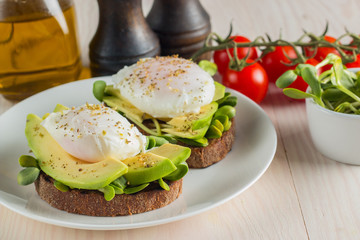 Avocado toast, cherry tomato and poached eggs on wooden background. Breakfast with vegetarian food, healthy diet concept.