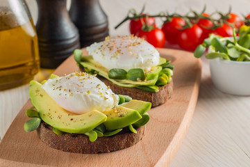 Avocado toast, cherry tomato and poached eggs on wooden background. Breakfast with vegetarian food, healthy diet concept.
