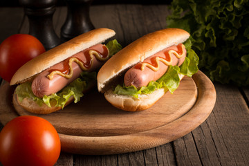 Photo of barbecue grilled hot dog with yellow mustard and ketchup on wooden background. Hot dog sandwich with potato fries and sauces.