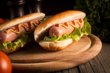 Photo of barbecue grilled hot dog with yellow mustard and ketchup on wooden background. Hot dog sandwich with potato fries and sauces.
