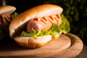 Photo of barbecue grilled hot dog with yellow mustard and ketchup on wooden background. Hot dog sandwich with potato fries and sauces.