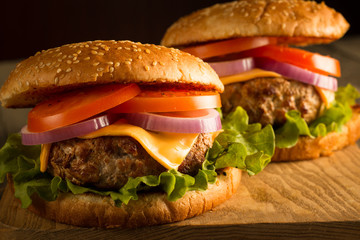 Home made hamburger with beef, onion, tomato, lettuce and cheese. Fresh burger close up on wooden rustic table with potato fries, beer and chips. Cheeseburger.