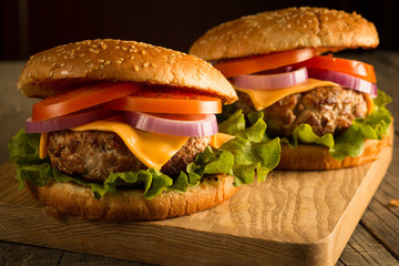 Home made hamburger with beef, onion, tomato, lettuce and cheese. Fresh burger close up on wooden rustic table with potato fries, beer and chips. Cheeseburger.