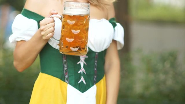 Bright young waitress in a national Bavarian suit with a mug of German beer in her hands makes a curtsy, bows and laughs cheerfully. The beer festival Oktoberfest