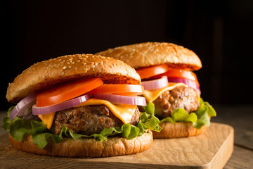 Home made hamburger with beef, onion, tomato, lettuce and cheese. Fresh burger close up on wooden rustic table with potato fries, beer and chips. Cheeseburger.