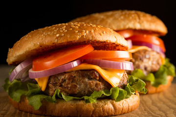 Home made hamburger with beef, onion, tomato, lettuce and cheese. Fresh burger close up on wooden rustic table with potato fries, beer and chips. Cheeseburger.