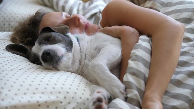 Girl And Her Pet Dog Hugging In The Bed.