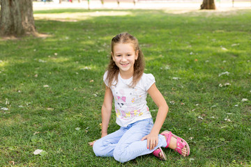 a little girl sitting on the lawn. girl in a white t-shirt and jeans. a walk in the Park. child