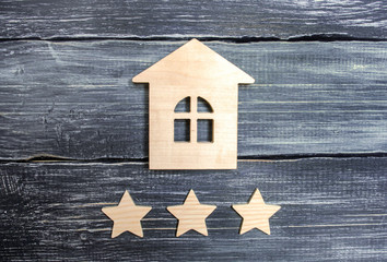 Wooden house and three stars on a gray background. Rating of houses and private property. Buying and selling, renting apartments. The level of the restaurant and hotels. Rating five stars.