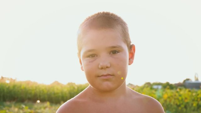 Portrait of a chubby boy with a black eye on the background of a green field, a child with a naked torso and a bruise on his face, low-key smile