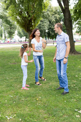 Naklejka na ściany i meble daughter mom and dad sitting on the lawn. in a white t-shirt and jeans. a walk in the Park. child. mom dad daughter. summer. family.