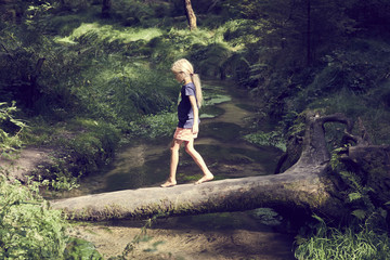 Child cute blond girl playing in the creek. Girl walking in forest stream and exploring nature. Summer children fun. Children summer activities