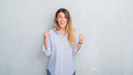 Young adult woman over grey grunge wall wearing fashion business outfit celebrating surprised and amazed for success with arms raised and open eyes. Winner concept.