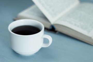 A cup of hot drink, coffee and an open book. 