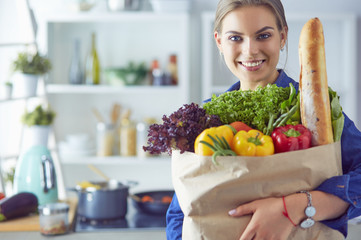 Young woman holding grocery shopping bag with vegetables .Standing in the kitchen