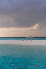 An idyllic island in Maldive in a stormy weather afternoon. Super clear water, white sand, traditional huts and tropical climate feeling.