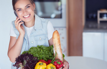 Smiling woman with mobile phone holding shopping bag in kitchen