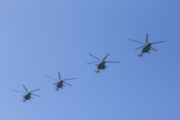 Several military helicopters fly side by side against the blue sky