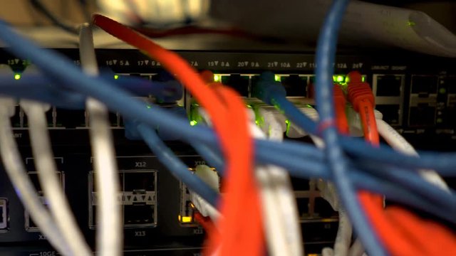 Scene tracks past the multi-colored cables and blinking green lights of a network Ethernet switch.