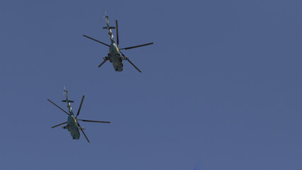 Several military helicopters fly side by side against the blue sky
