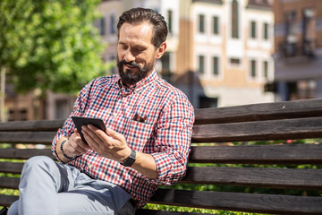 Obraz premium Pleasant adult man reading his e-book on the bench