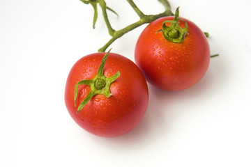 Two tomatoes with leaf isolated on white background. While tomatoes are botanically berry-type fruits, they are considered culinary vegetables as an ingredient or side dish for savory meals.