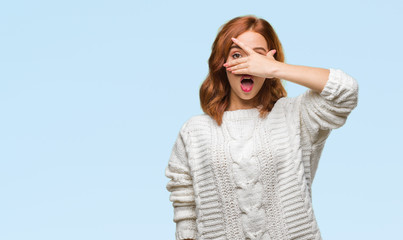 Young beautiful woman over isolated background wearing winter sweater peeking in shock covering face and eyes with hand, looking through fingers with embarrassed expression.