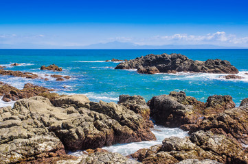 Fototapeta na wymiar Beautiful view of beach with rock formations in the ocean with waves approaching and blue sky near sand and forest